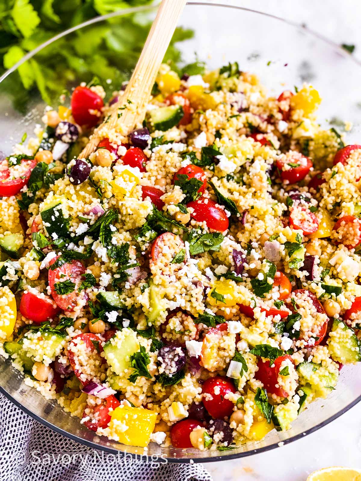 couscous frontal view of couscous salad in glass bowl with wooden spoon stuck in salad