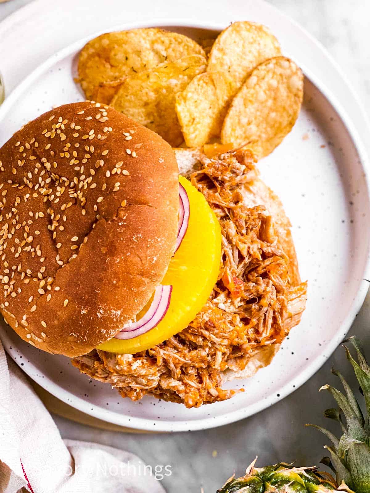 overhead view of pineapple pulled pork sandwich with chips on white plate