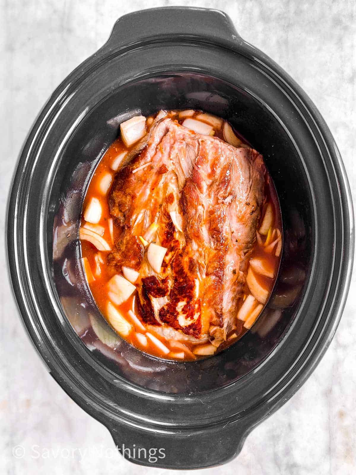 browned pork neck with raw onion and pineapple BBQ sauce in black crock