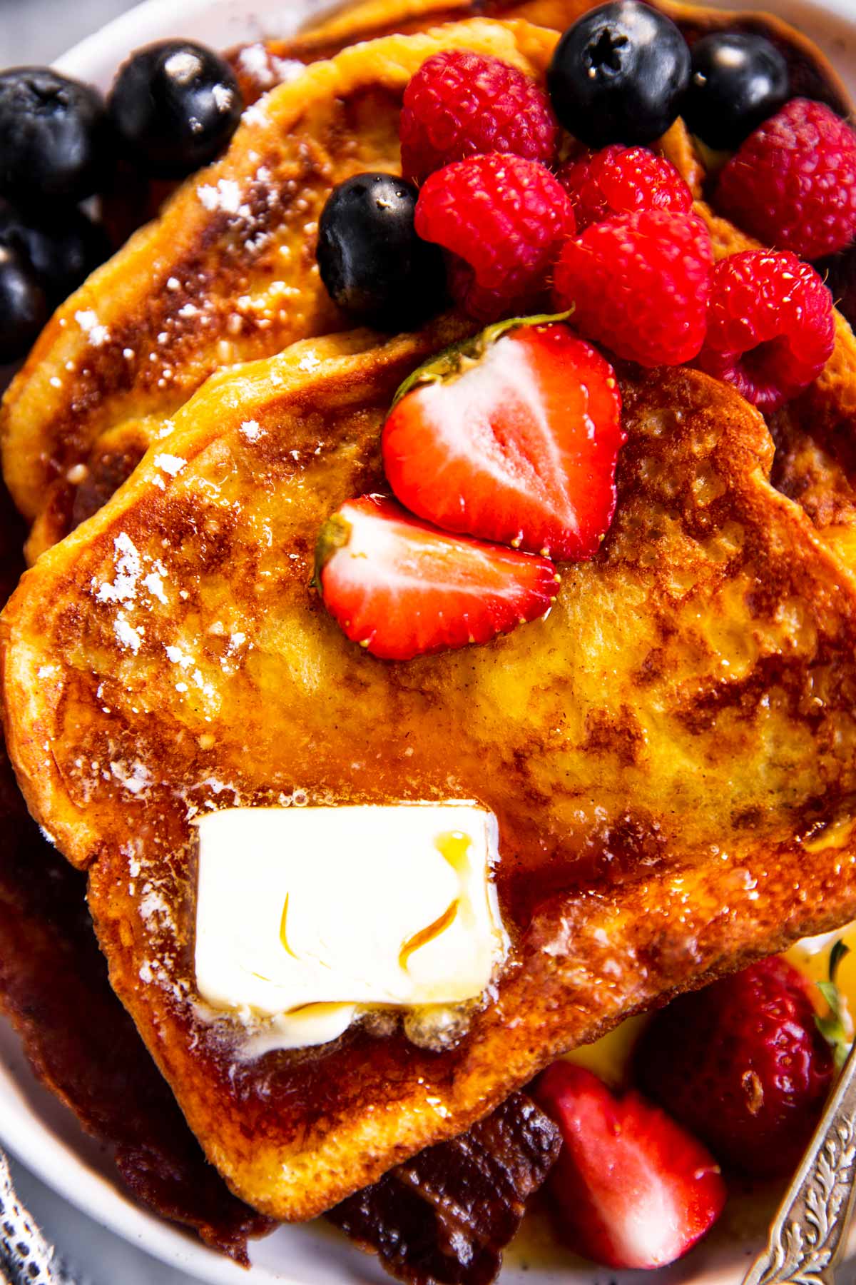 close up photo of French toast on plate with butter, maple syrup and fresh berries