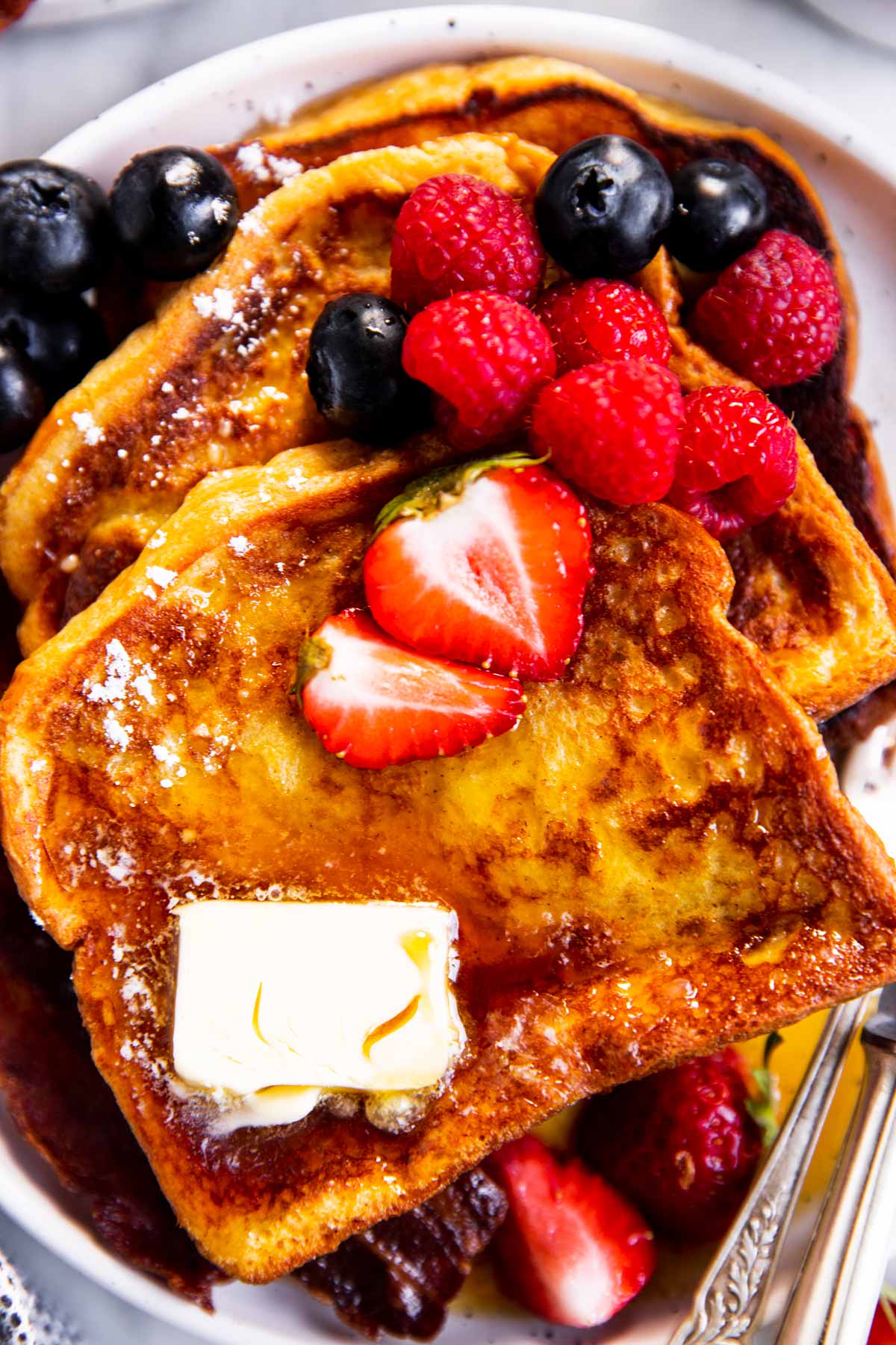 overhead view of slices of French toast garnished with icing sugar, butter and berries