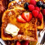 three slices of French toast on white plate with butter, bacon and berries