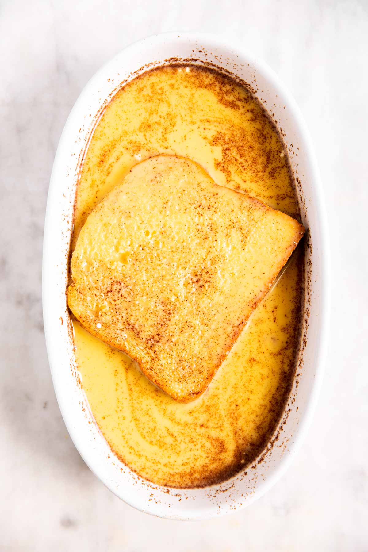 slice of brioche in egg mixture inside oval white casserole dish