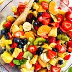 overhead view of fresh fruit salad in glass bowl with wooden spoon