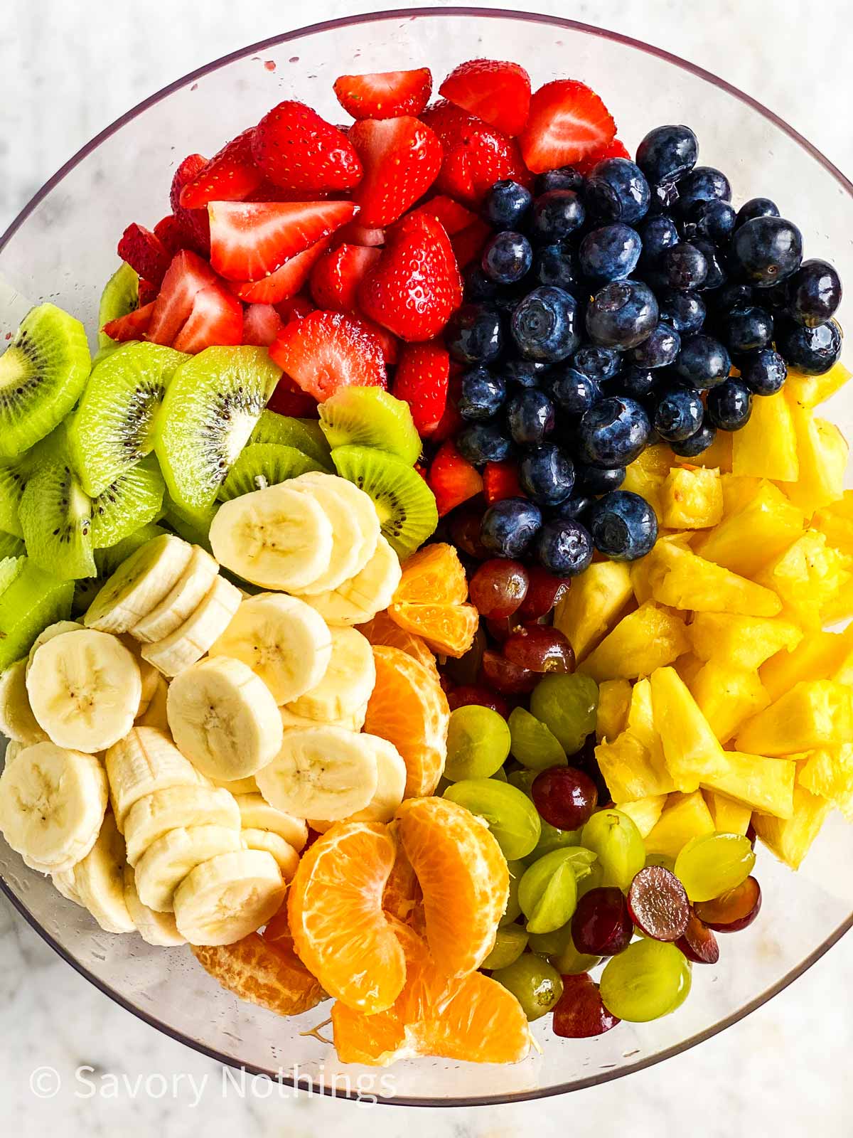 cut up fruit for fruit salad in large glass bowl