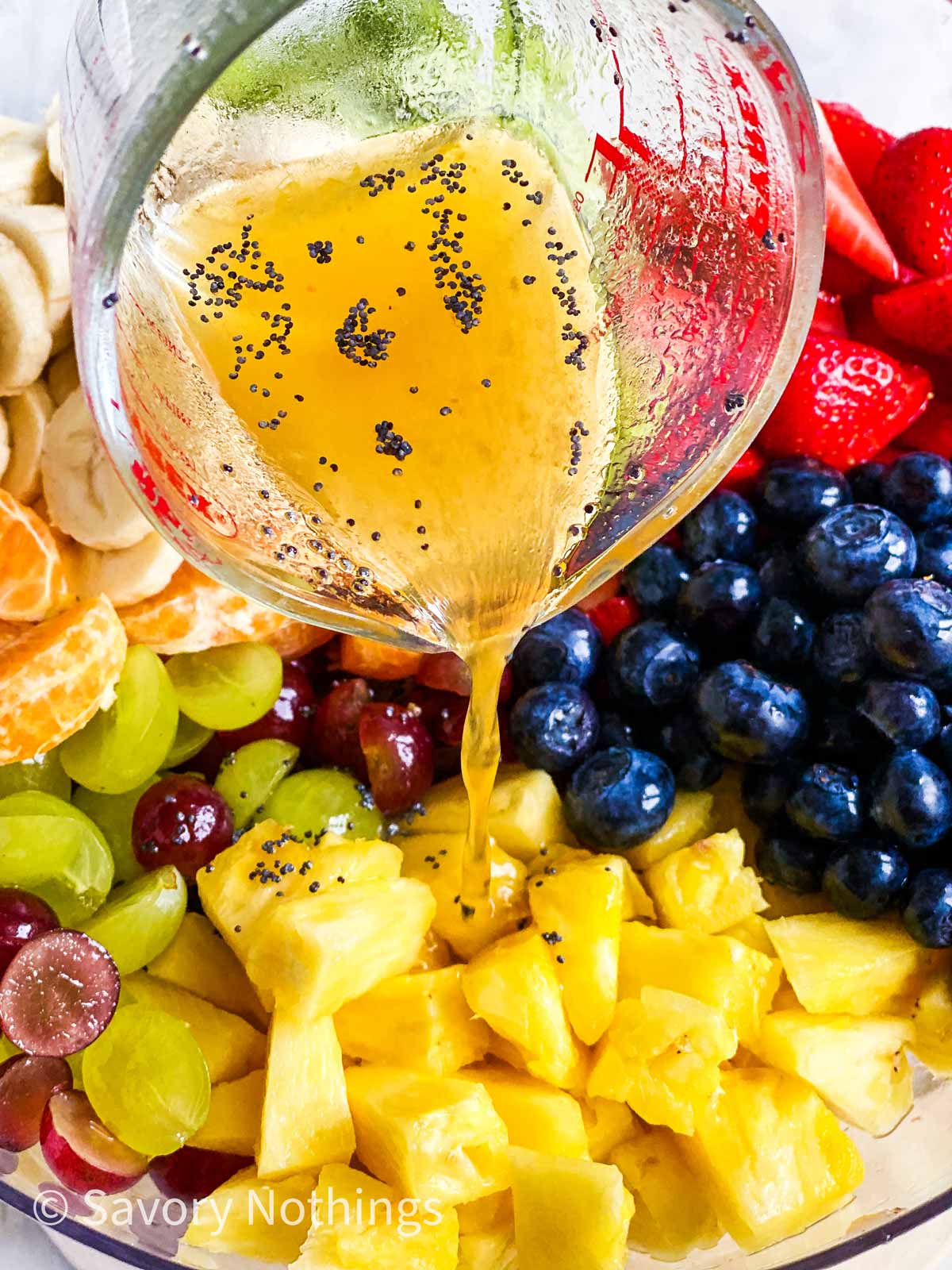 poppy seed fruit salad dressing pouring over fresh fruit in glass bowl