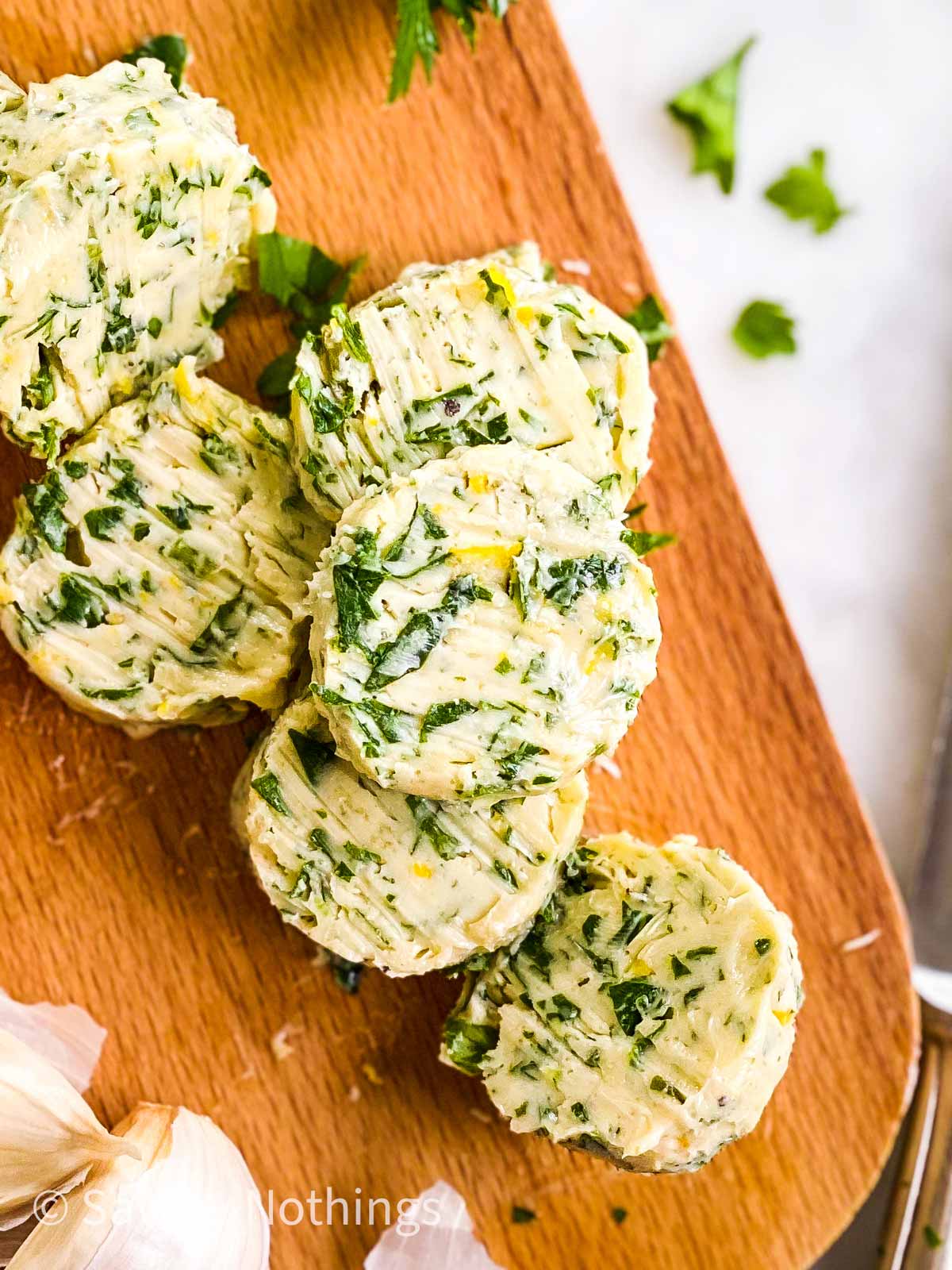 overhead view of sliced garlic herb butter on wooden board