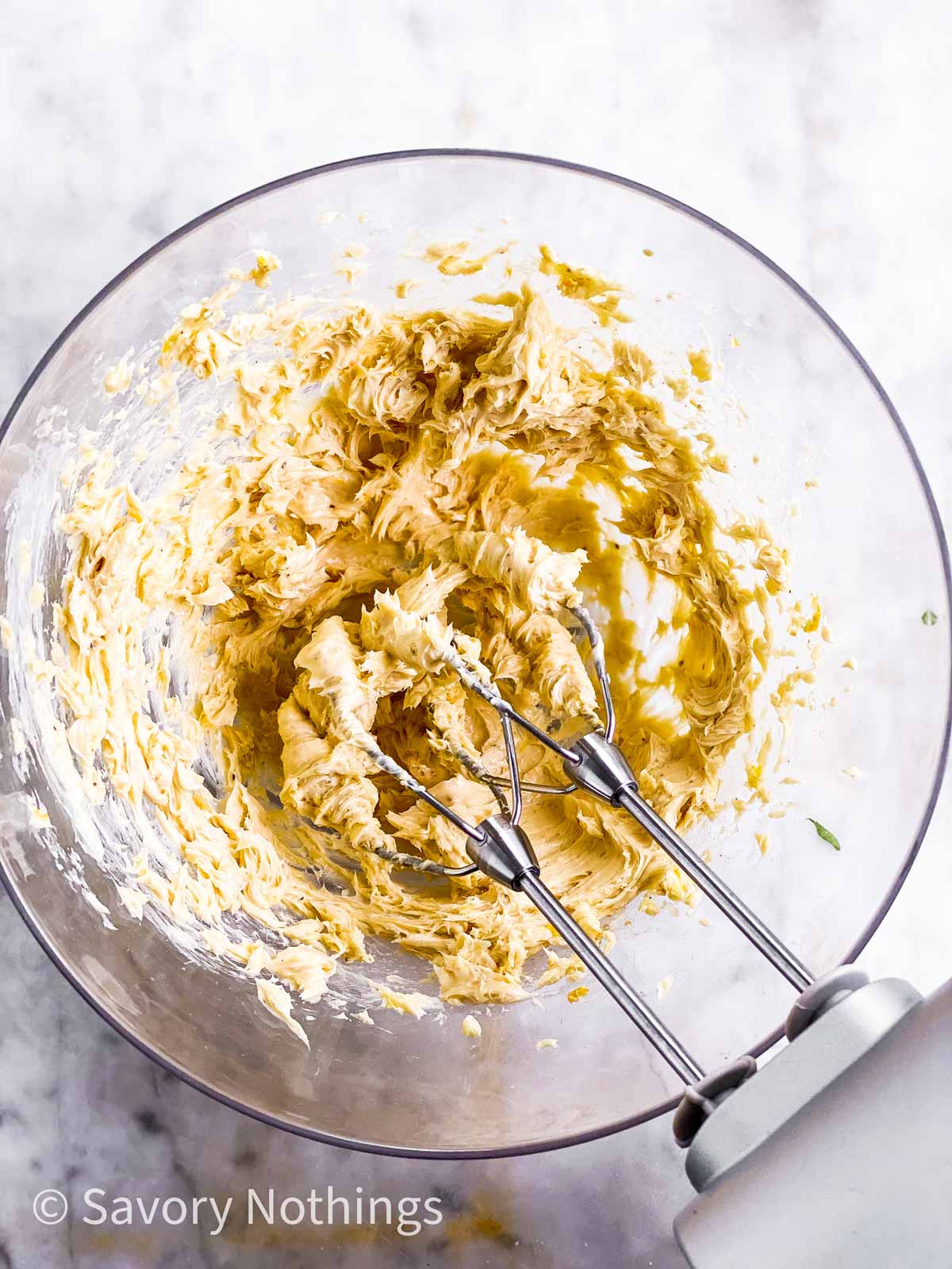 whipped garlic butter in glass bowl with beaters from hand mixer