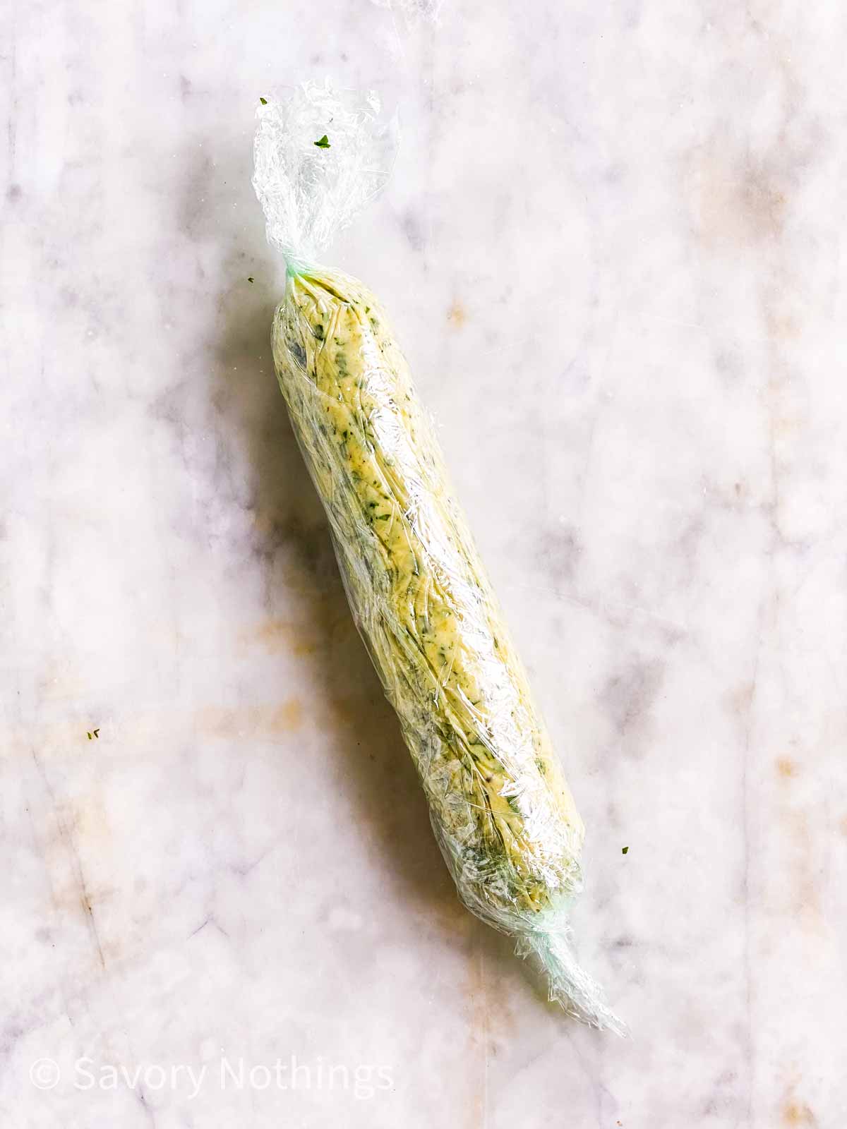 garlic herb butter wrapped in sausage shape in plastic wrap on marble surface