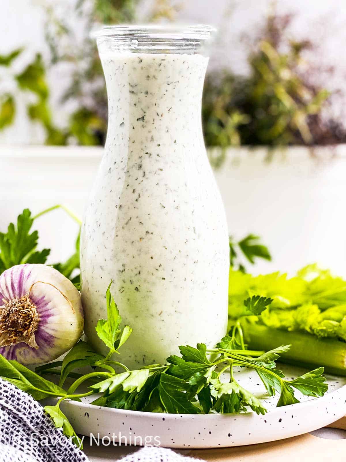 homemade ranch salad dressing in glass bottle on plate with fresh herbs and garlic