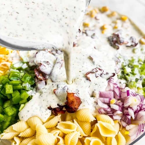 homemade ranch salad dressing pouring from glass measuring jug over salad ingredients