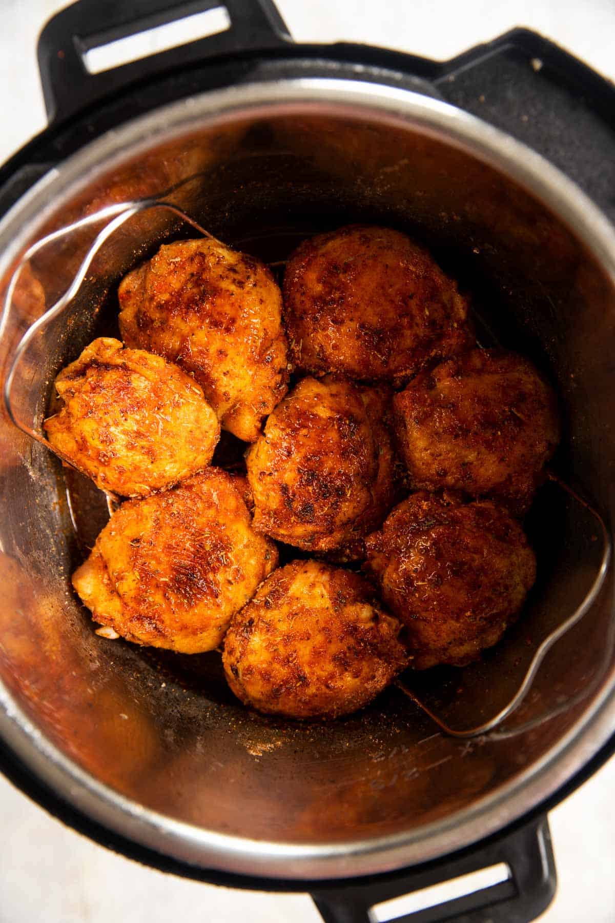 browned and seasoned chicken thighs in instant pot on top of trivet