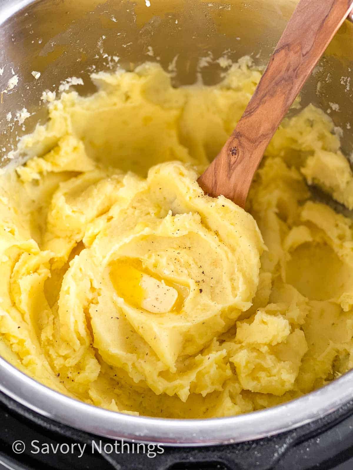 close up photo of mashed potatoes with butter in instant pot with wooden cooking spoon