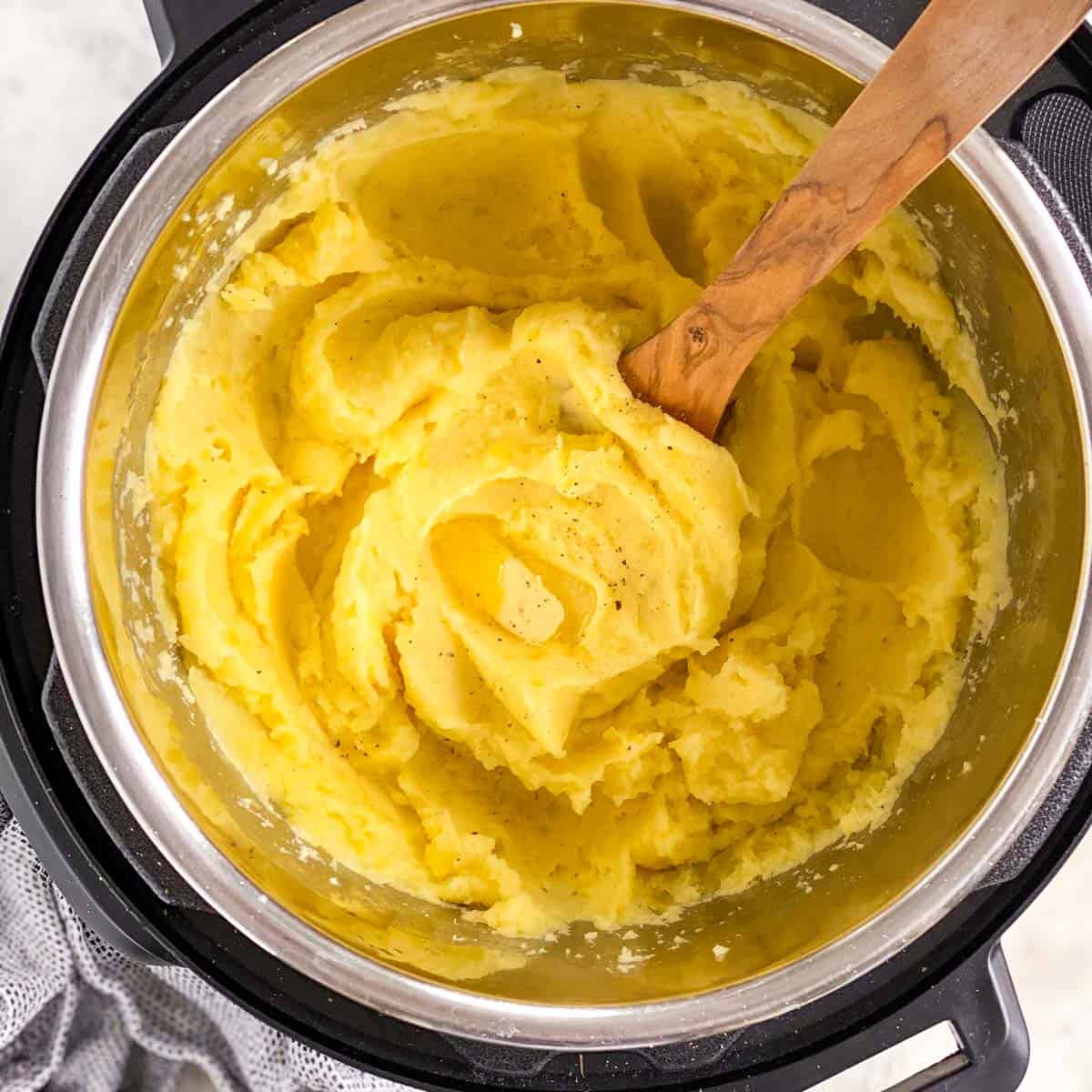 overhead view of mashed potatoes in instant pot with butter and wooden spoon stuck inside