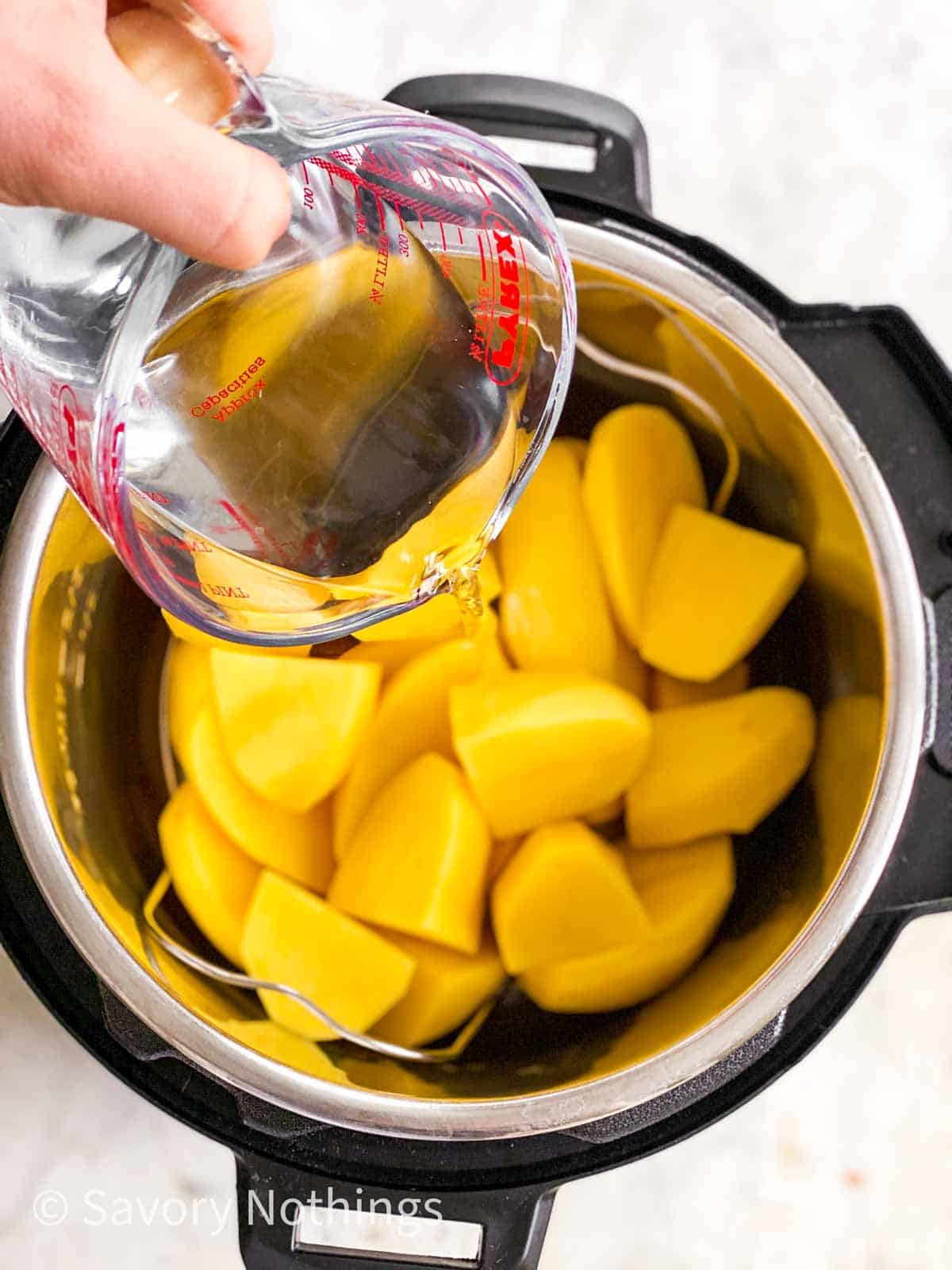 female hand pouring water into instant pot filled with curt up potatoes