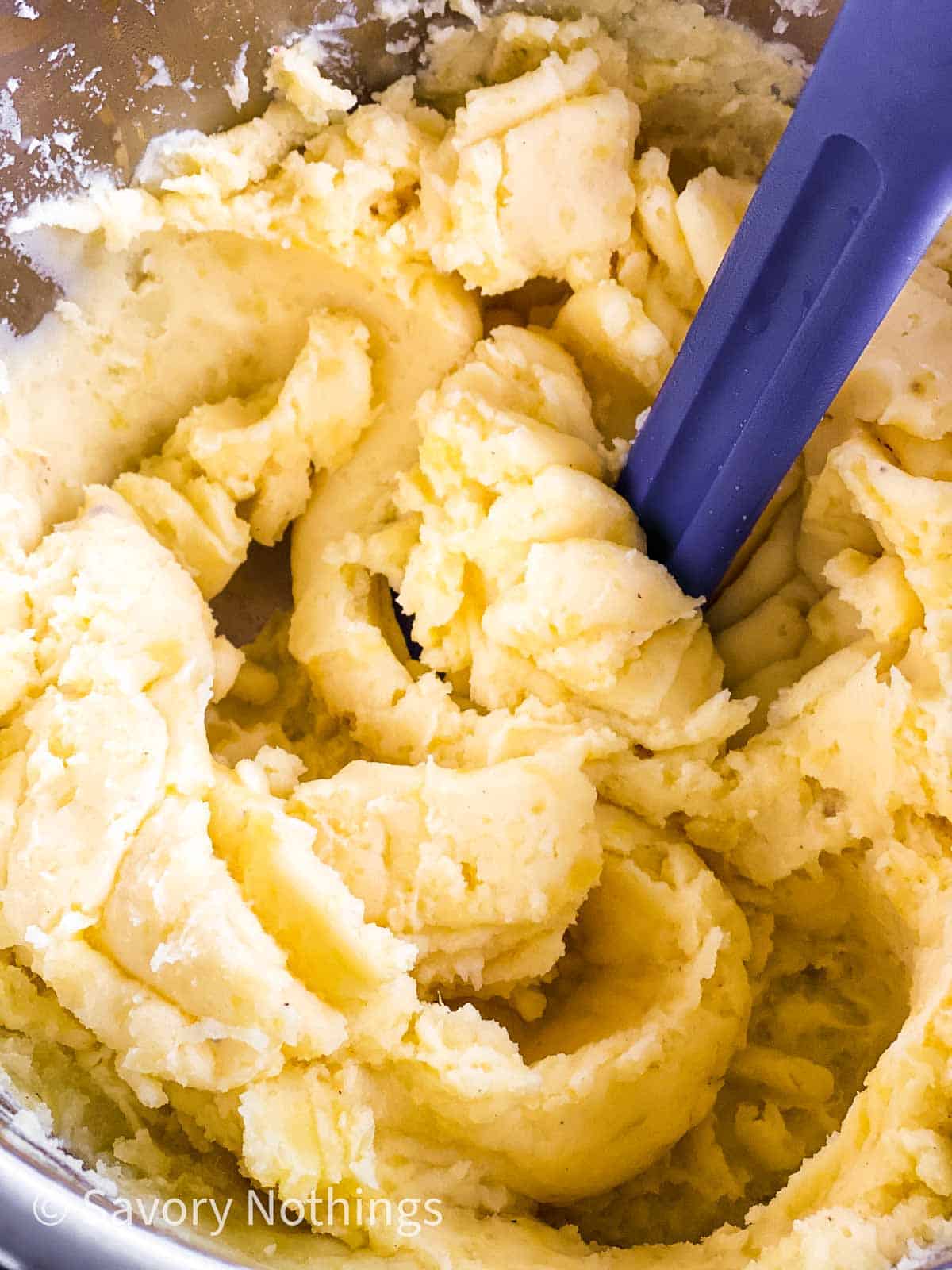 close up photo blue plastic potato masher stuck in mashed potatoes