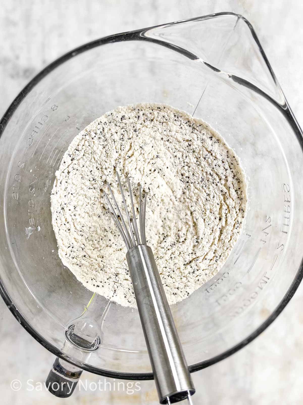 overhead view of dry ingredients for lemon poppy seed muffins in glass bowl with whisk