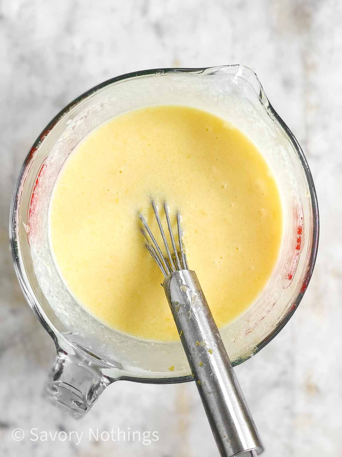 overhead view of wet ingredients for lemon poppy seed muffins in glass measuring cup with whisk