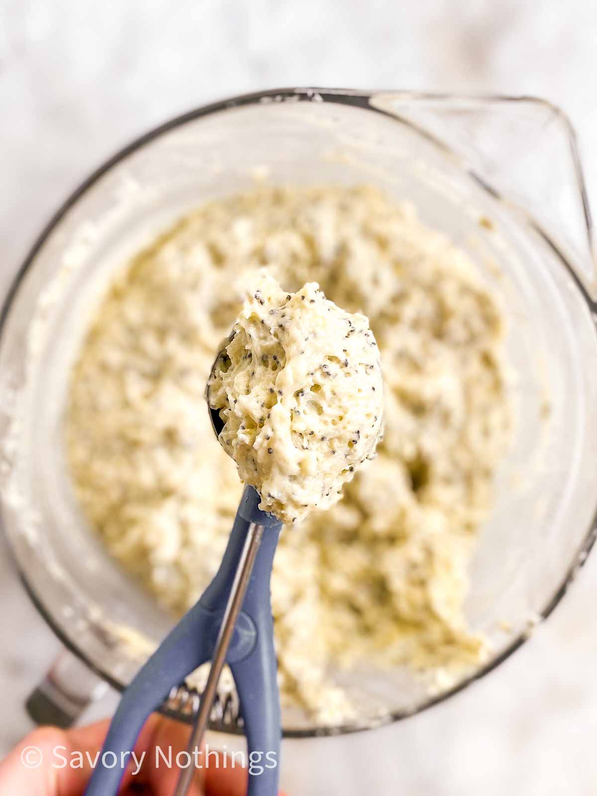 female hand holding ice cream scoop filled with muffin batter over bowl