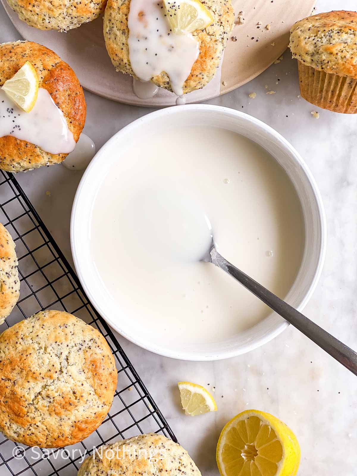overhead view of lemon glaze in white bowl surrounded by lemon poppy seed muffins
