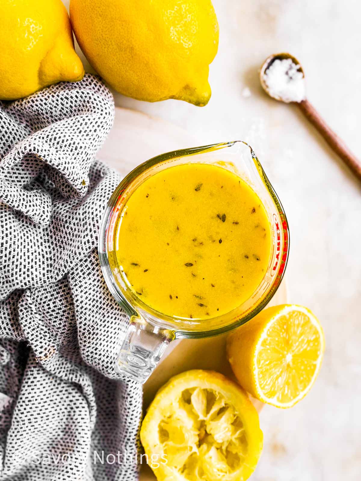 overhead view of lemon vinaigrette in glass measuring jug surrounded by fresh lemons and spoonful of salt