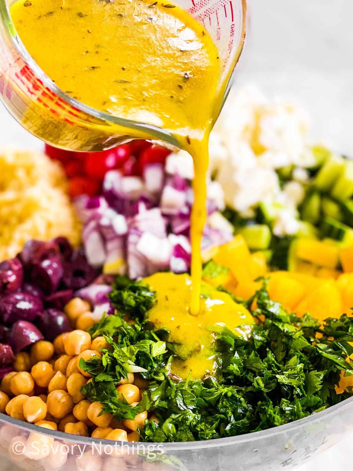 lemon vinaigrette pouring over salad ingredients from glass measuring jug