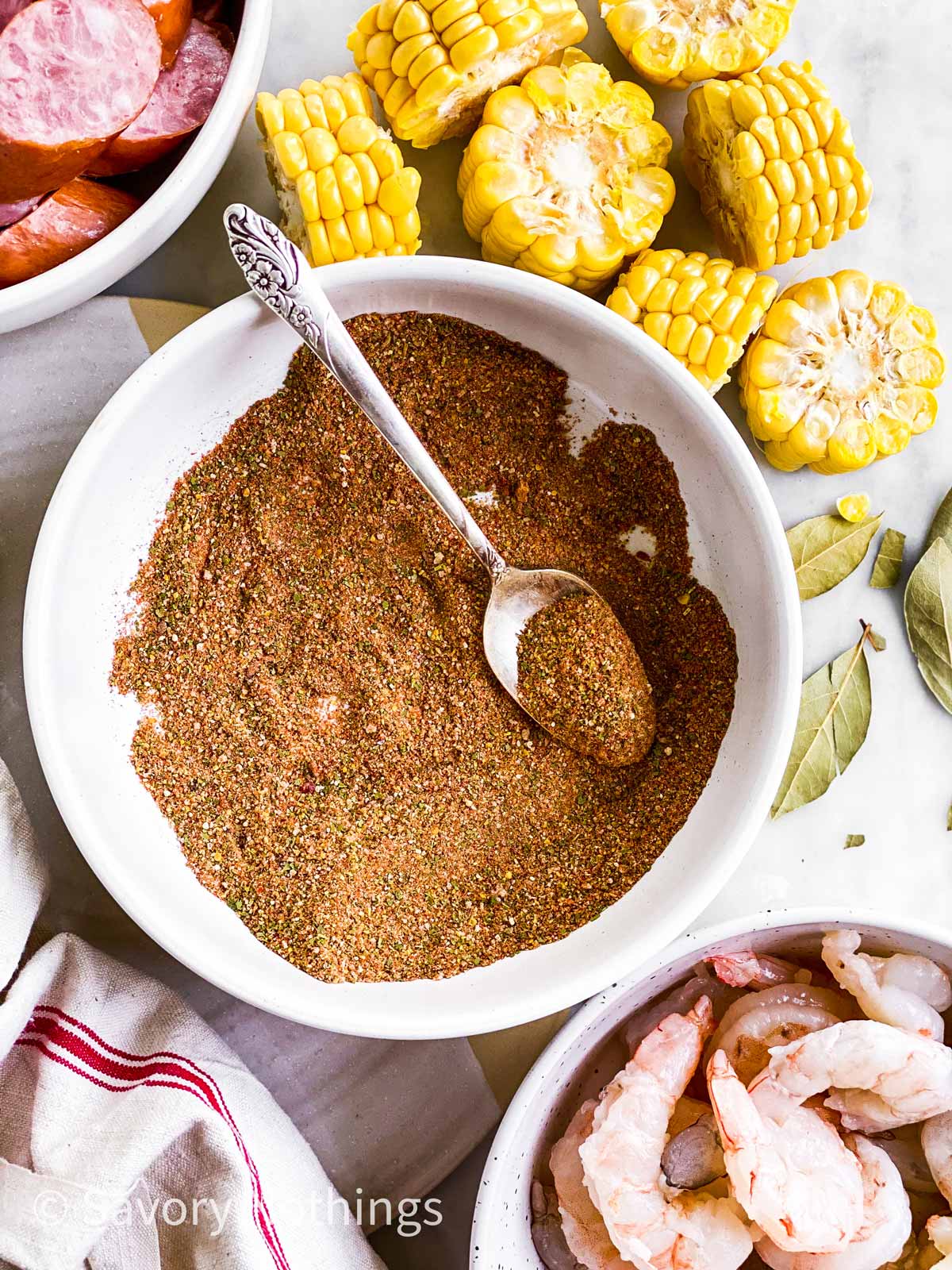 bowl with copycat old bay seasoning mix surrounded by raw shrimp, smoked sausage and corn on the cob