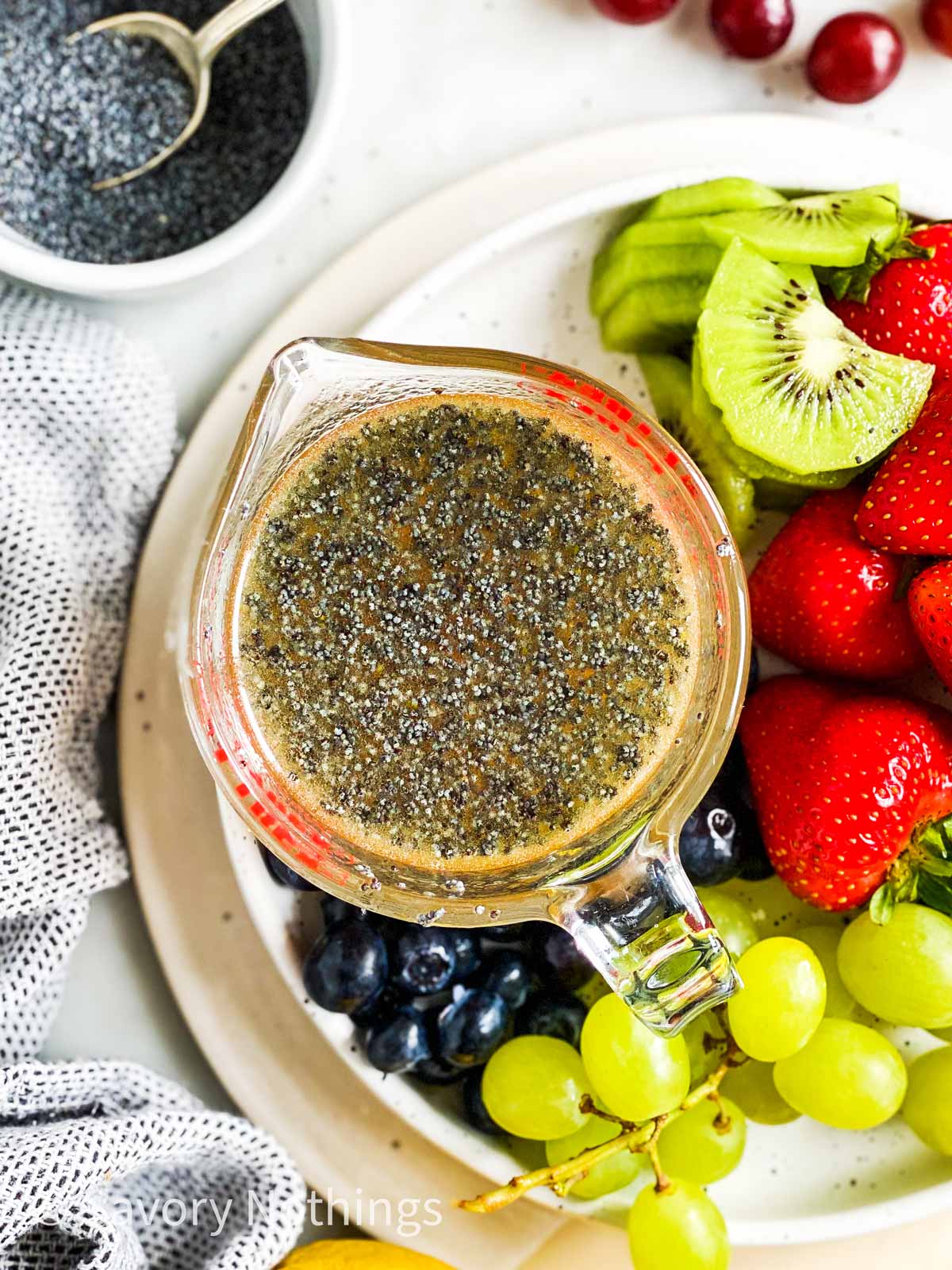 overhead view of poppy seed fruit salad dressing in glass measuring jug ob platter with fresh fruit