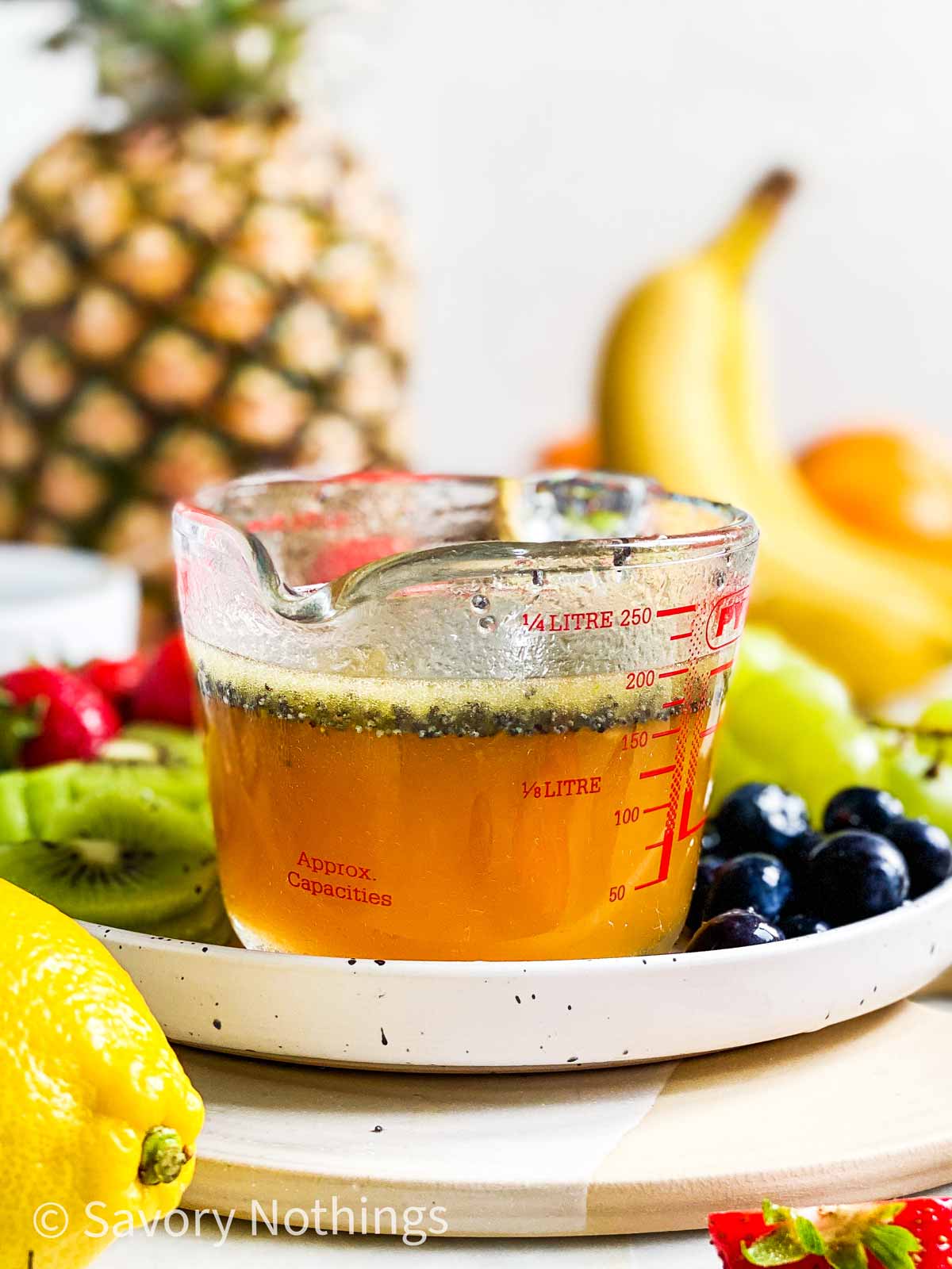 poppy seed fruit salad dressing in small glass measuring jug on platter with cut up fruit