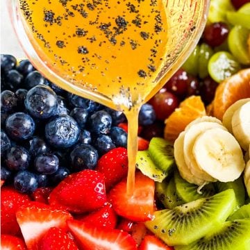 poppy seed fruit salad dressing pouring over freshly cut fruit from small glass measuring jug