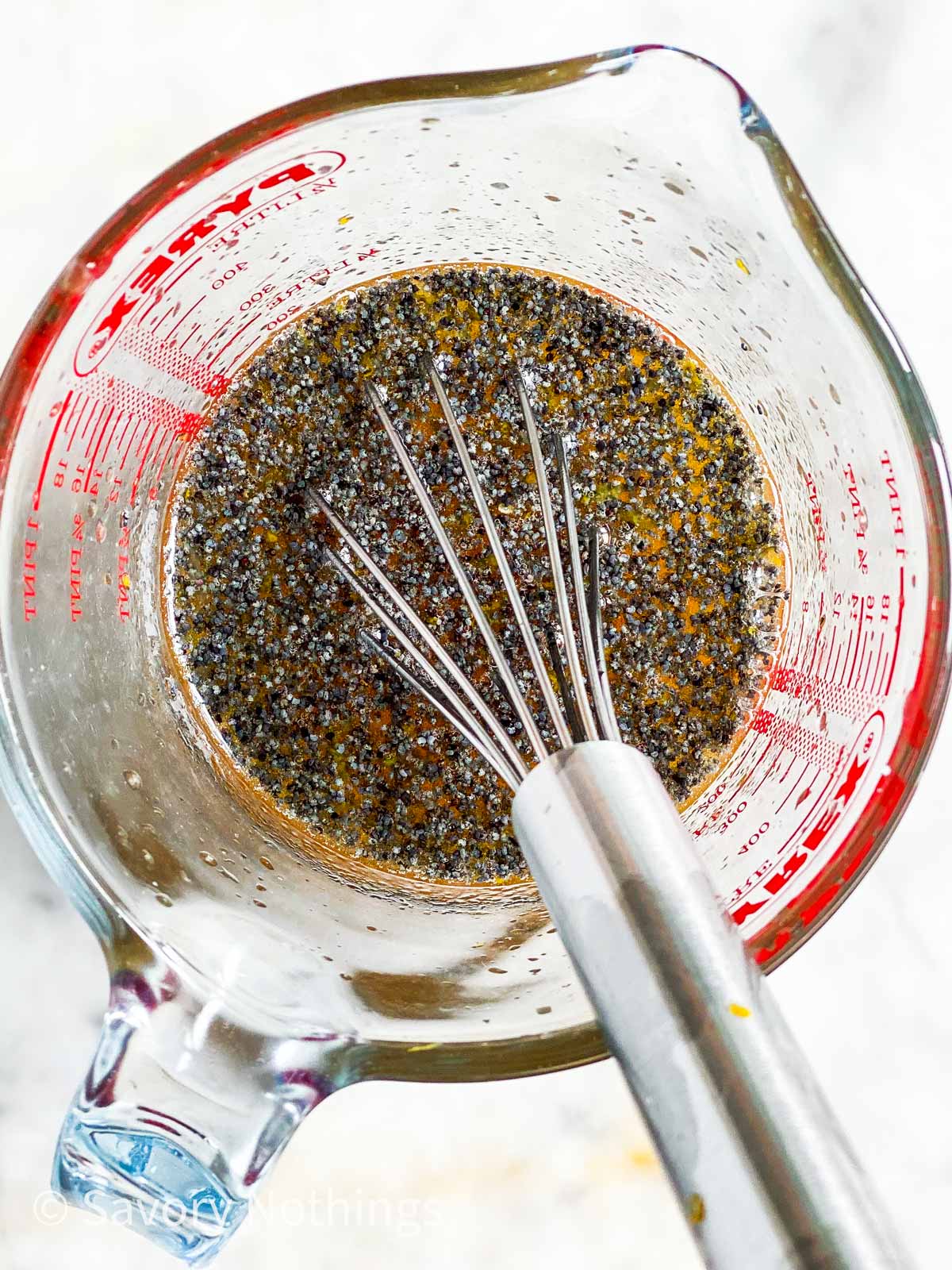 overhead view of poppy seed fruit salad dressing in glass measuring jug with metal whisk