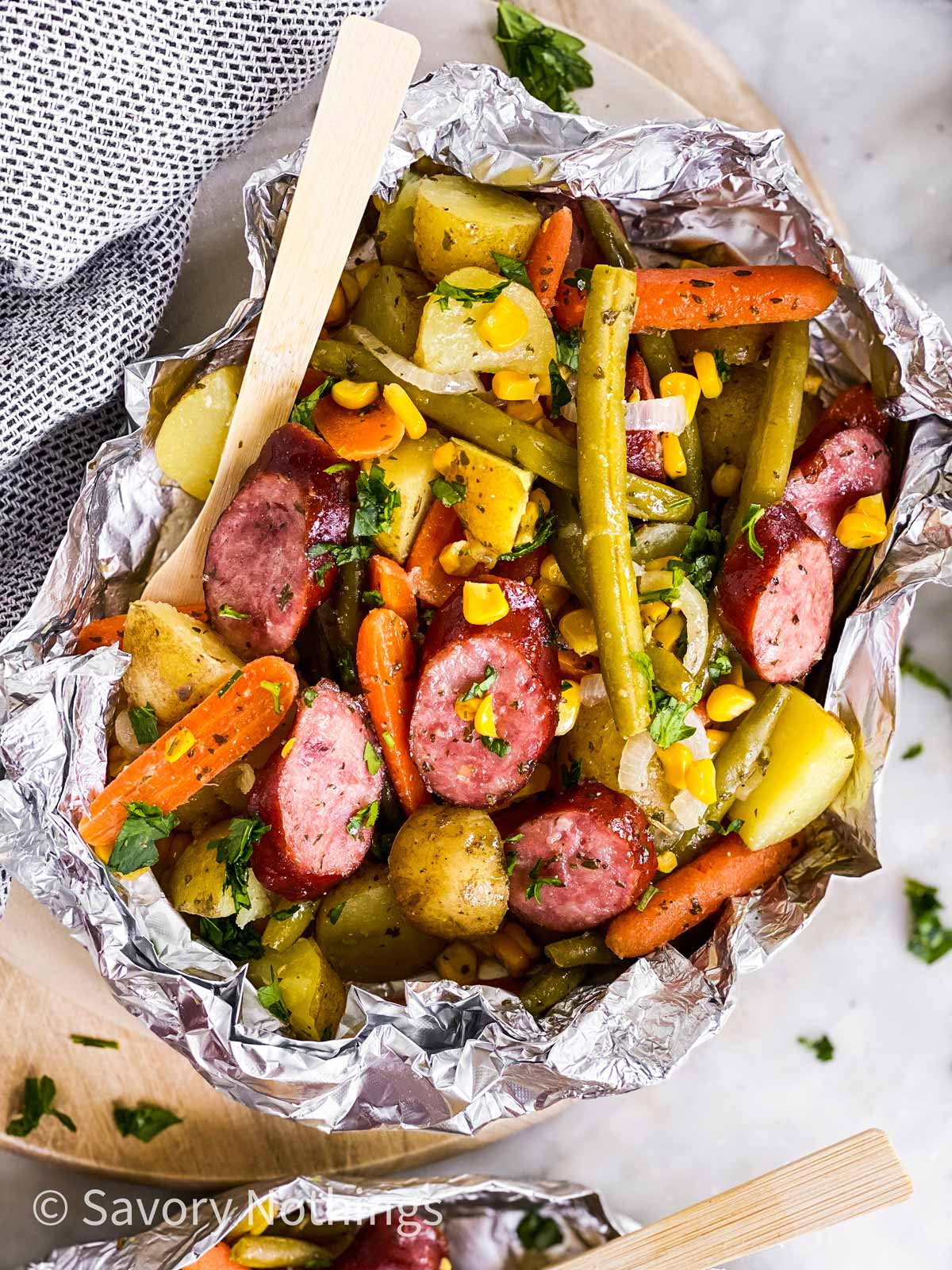 overhead view of opened sausage foil packet with wooden fork stuck inside