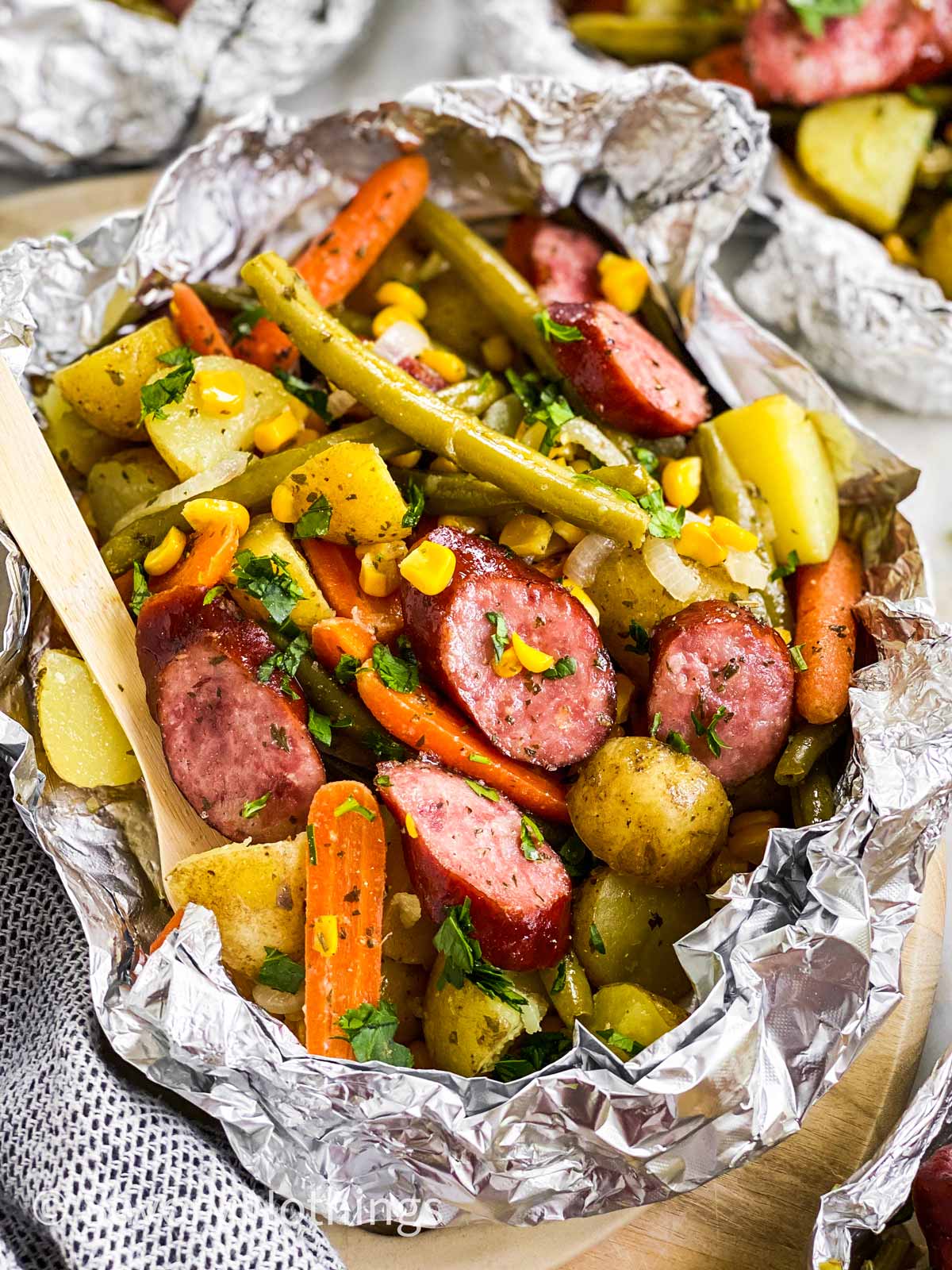 angled frontal view of sausage an potato foil packet garnished with chopped parsley