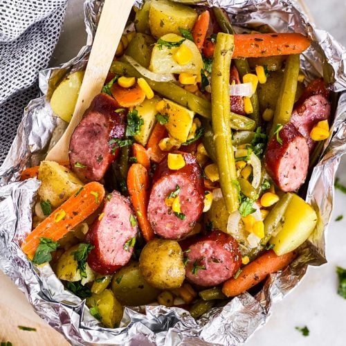 overhead close up view of opened sausage foil packet with bamboo fork stuck in