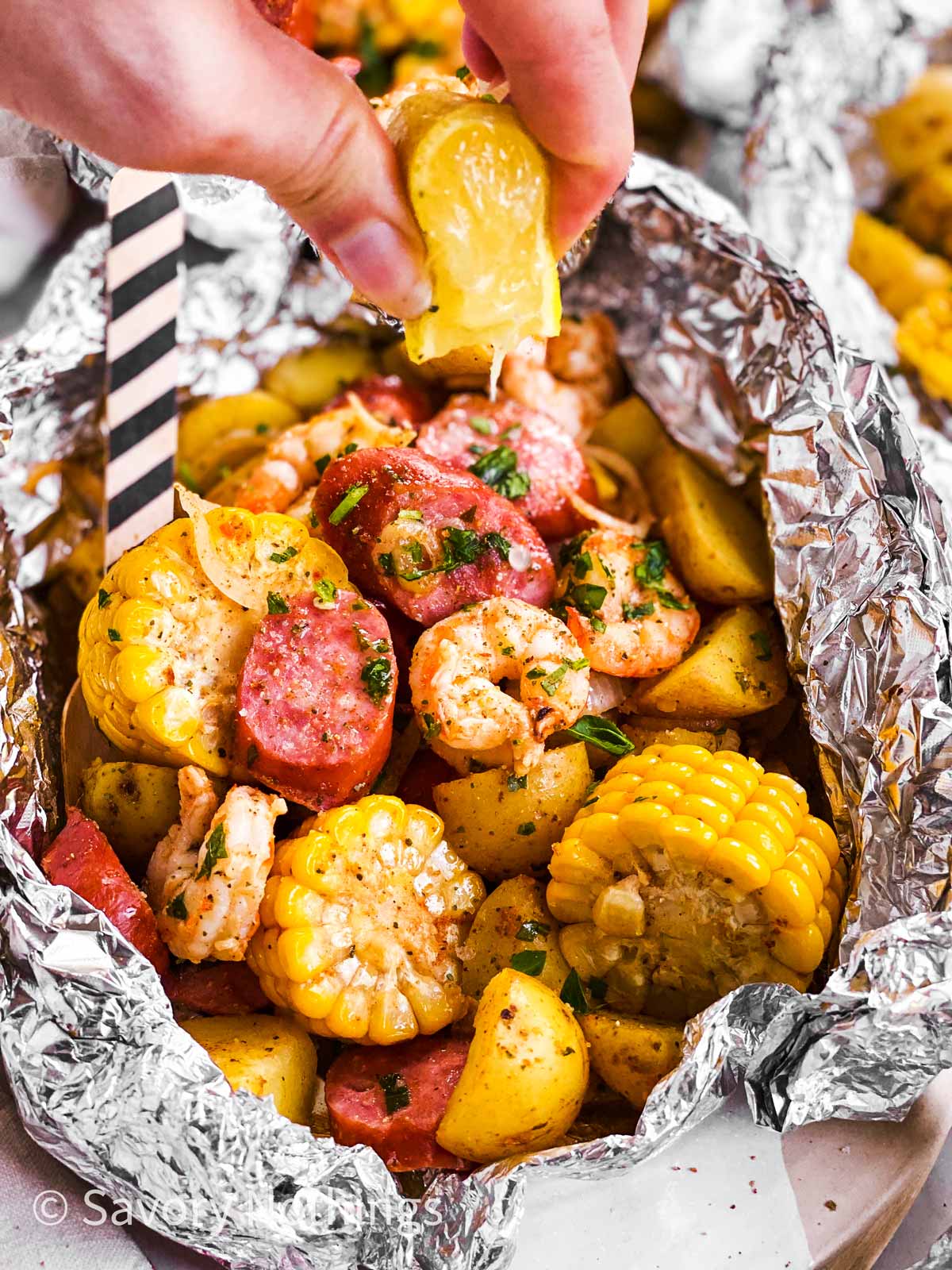 female hand drizzling lemon juice over shrimp boil foil packet