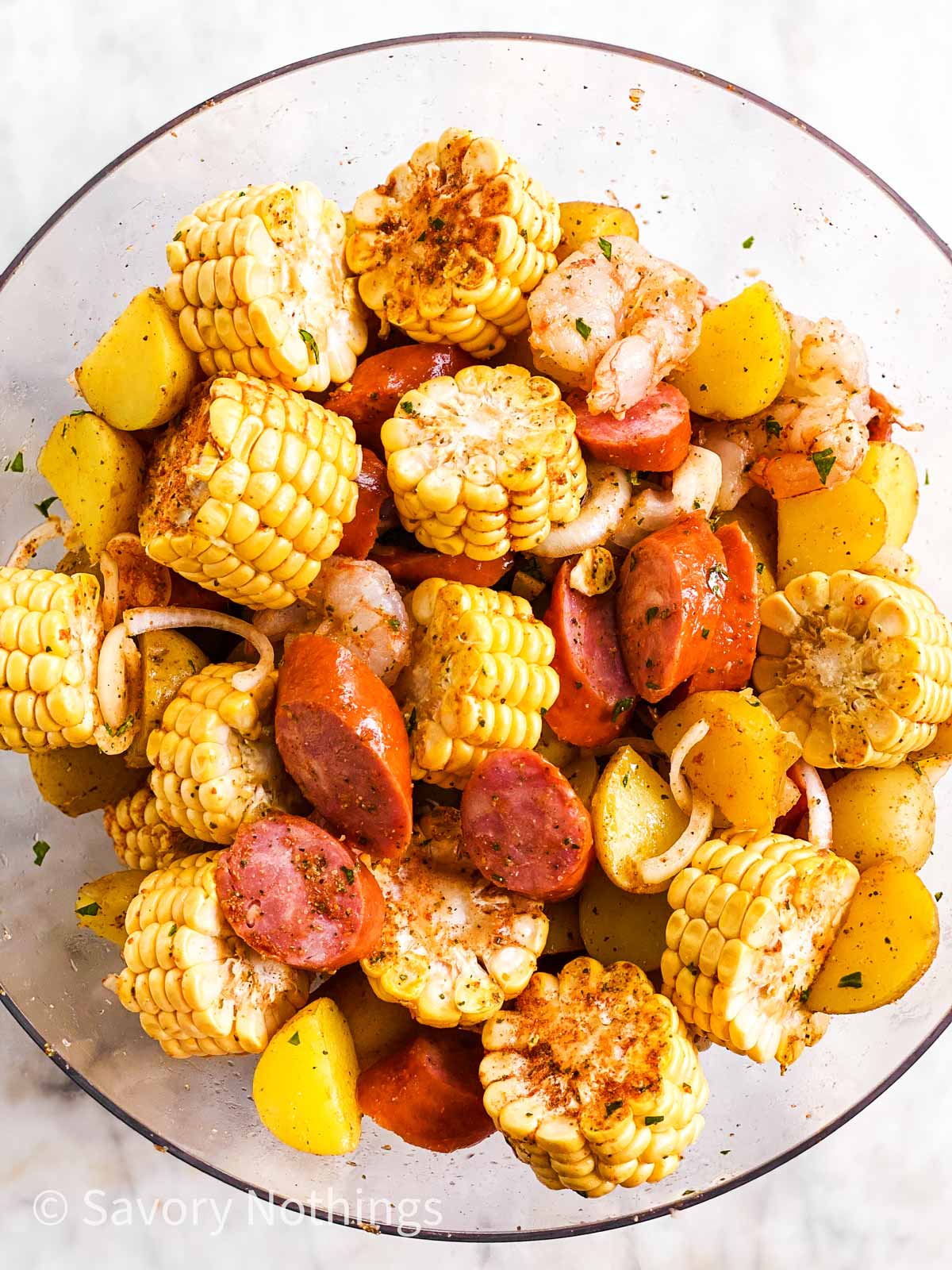 ingredients for shrimp boil foil packets combined in large glass bowl