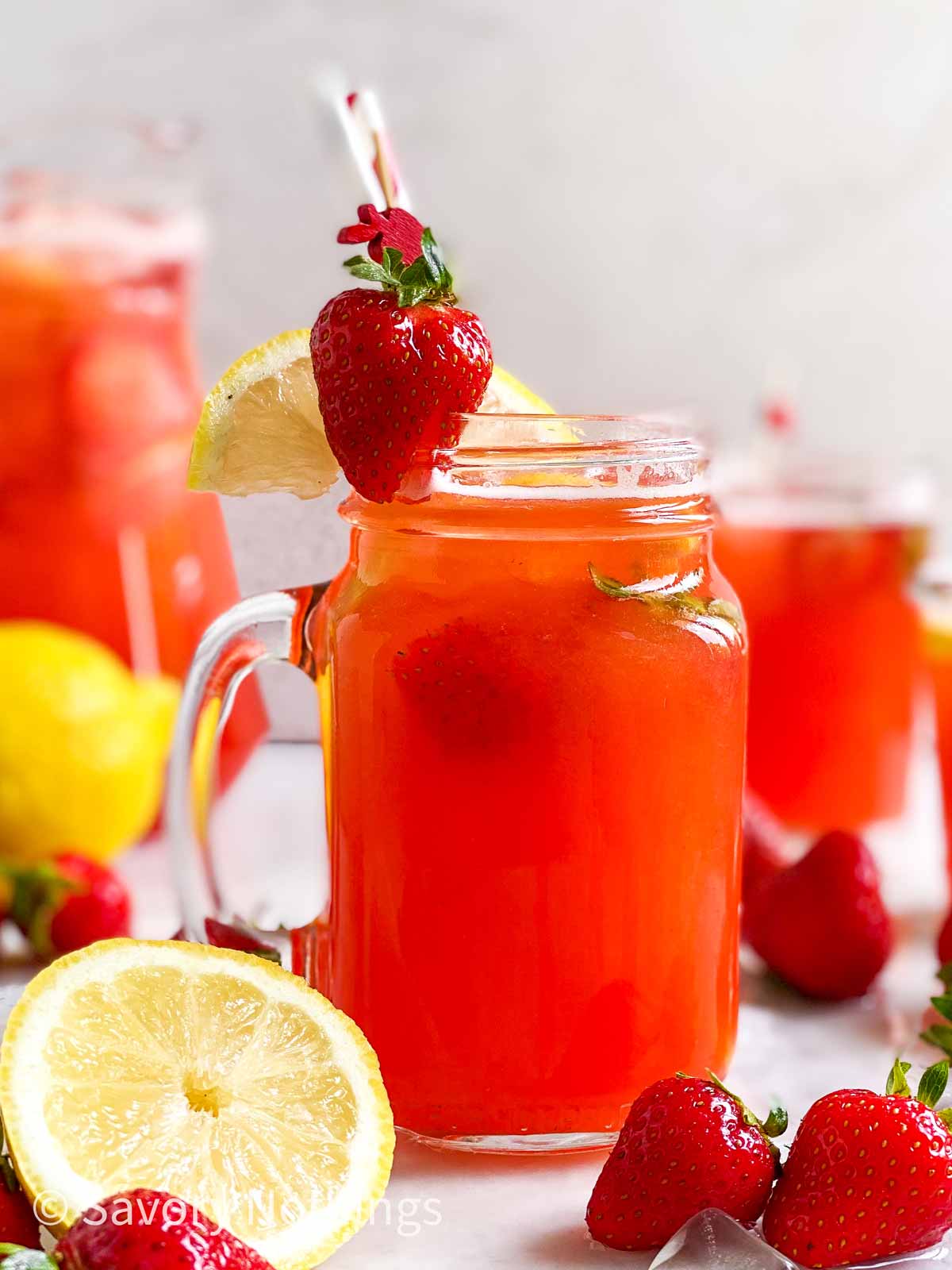 mason jar filled with strawberry lemonade and garnished with straws, fresh strawberries, ice and lemon