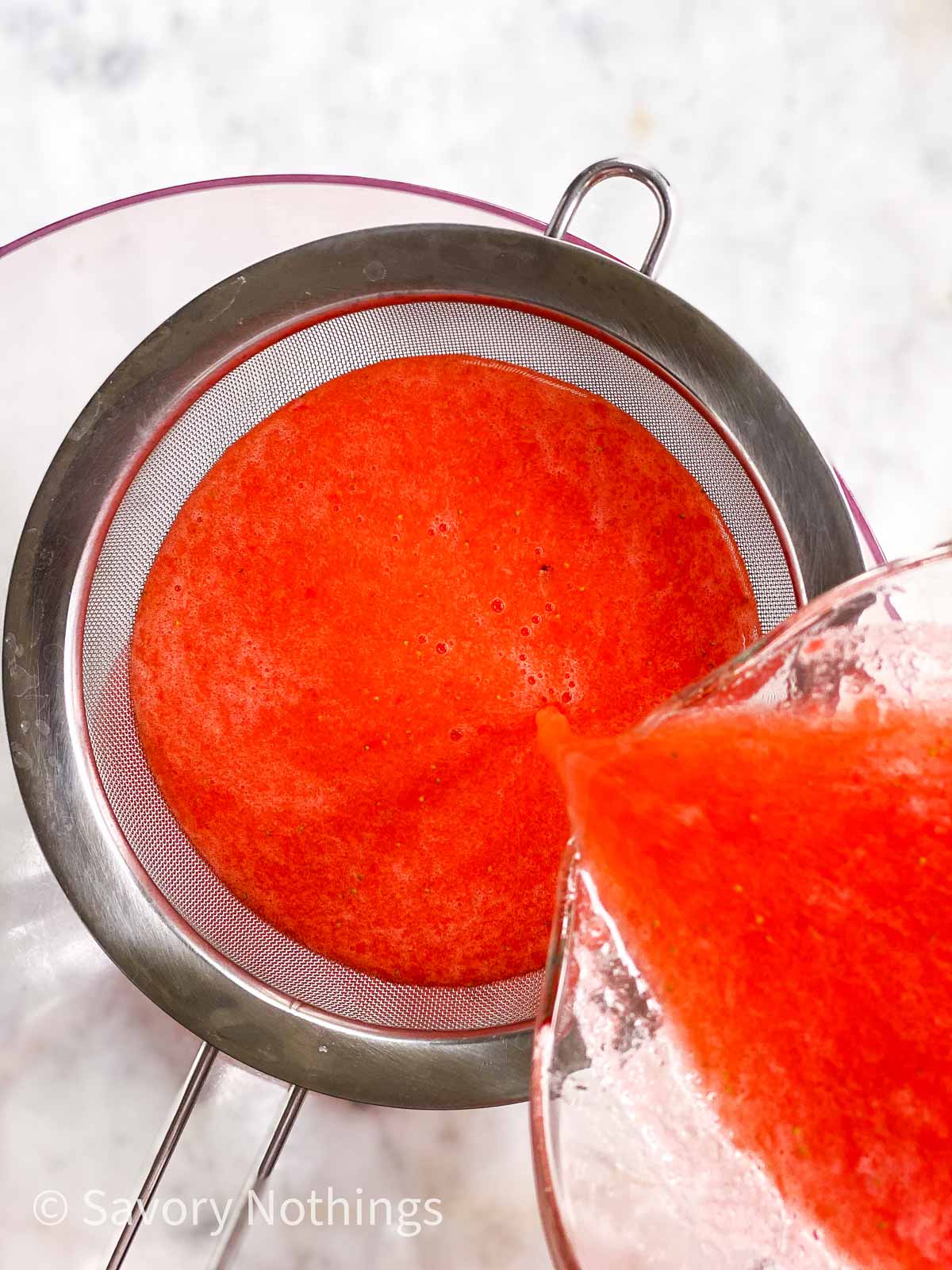 blended strawberries pouring through fine mesh sieve into glass bowl