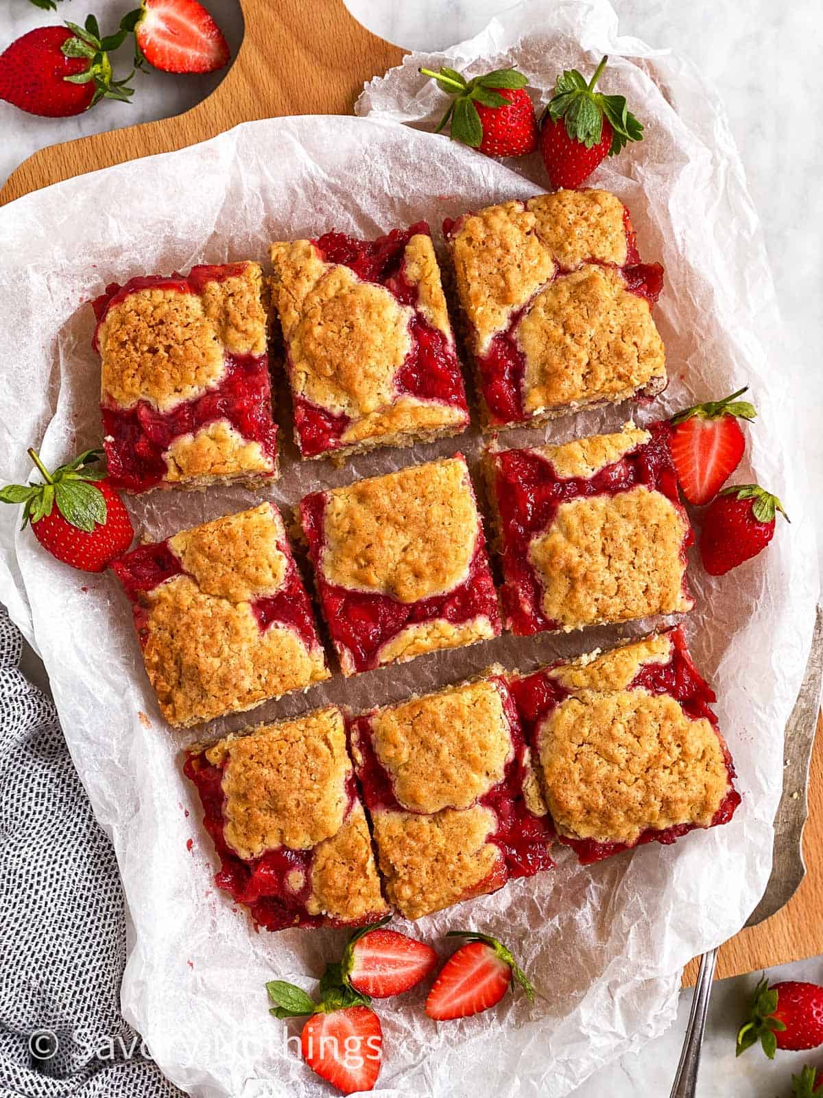 sliced strawberry oatmeal bars on white baking parchment surrounded by fresh strawberries 