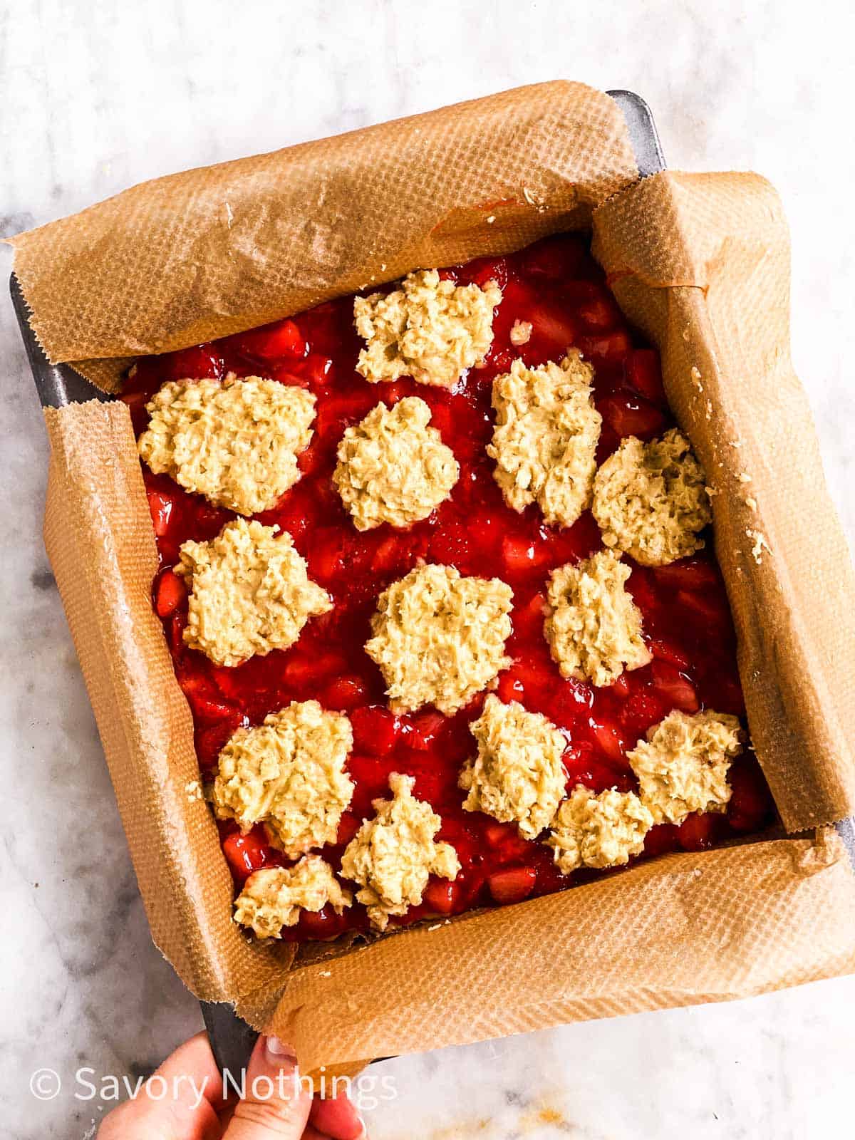 assembled, unbaked strawberry oatmeal bars in square pan lined with brown baking parchment