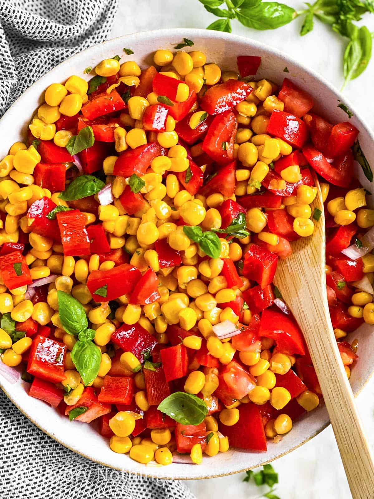 overhead close up view of summer corn salad in white bowl with wooden spoon