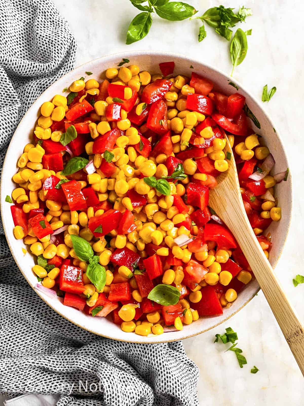 overhead view of summer corn salad in white bowl with wooden spoon