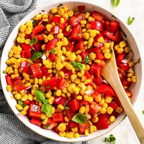 overhead view of summer corn salad in white bowl with wooden spoon