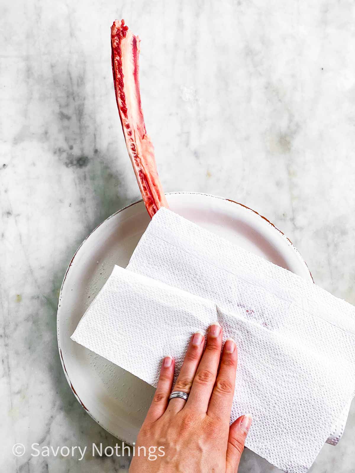 female hand using paper towels to pat dry a tomahawk steak on a white plate