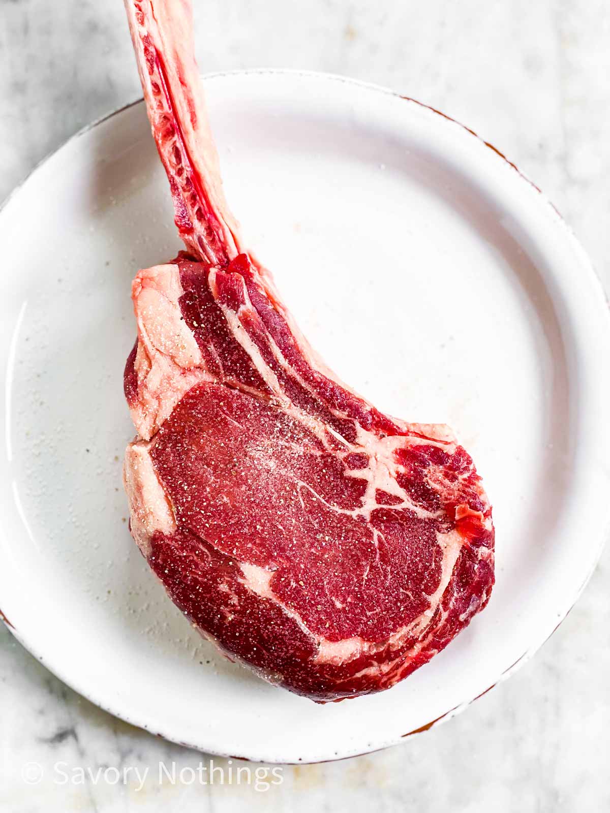 tomahawk steak on white plate, seasoned with salt and pepper