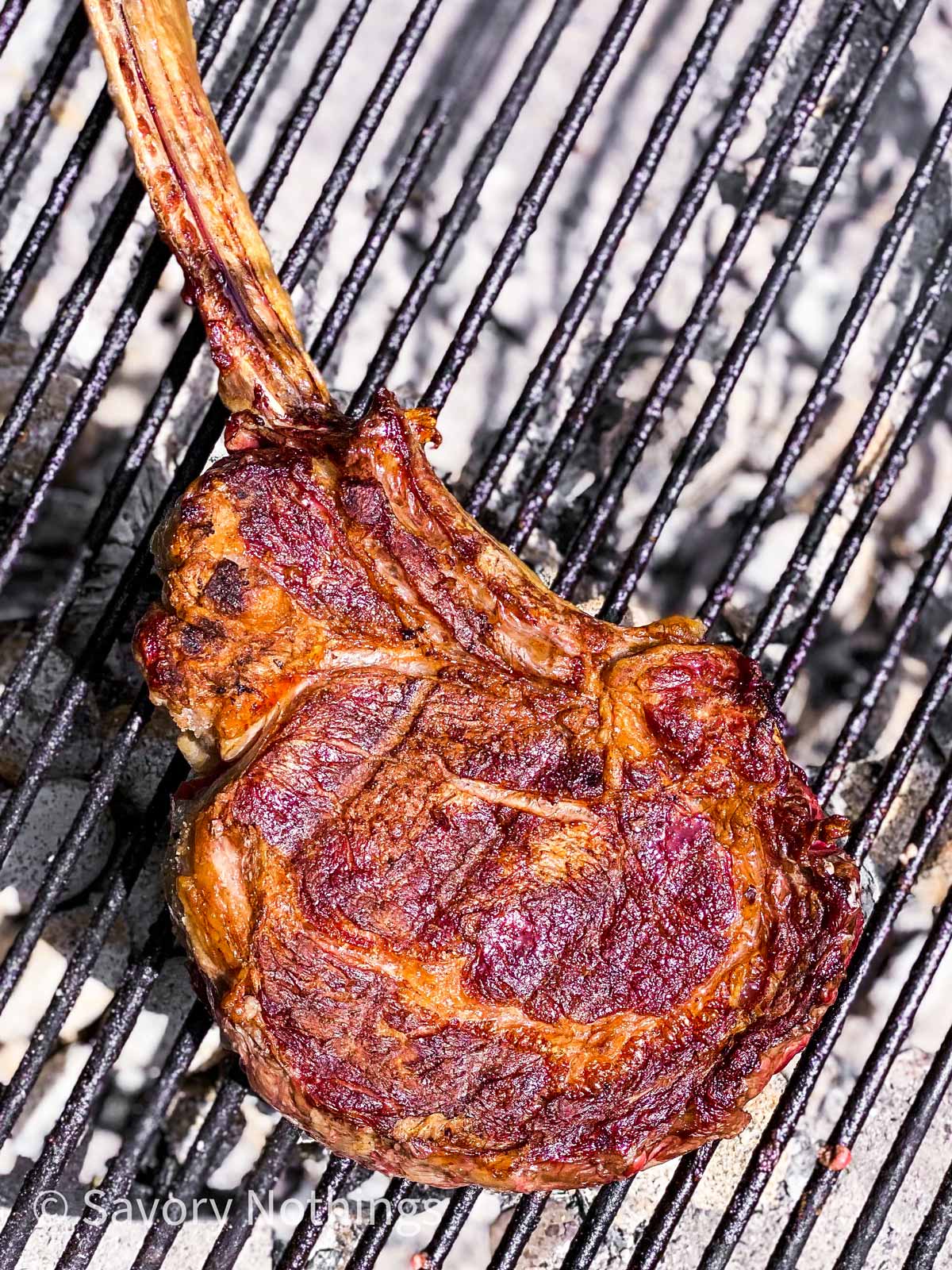 grilled tomahawk steak on grilling rack over hot coal