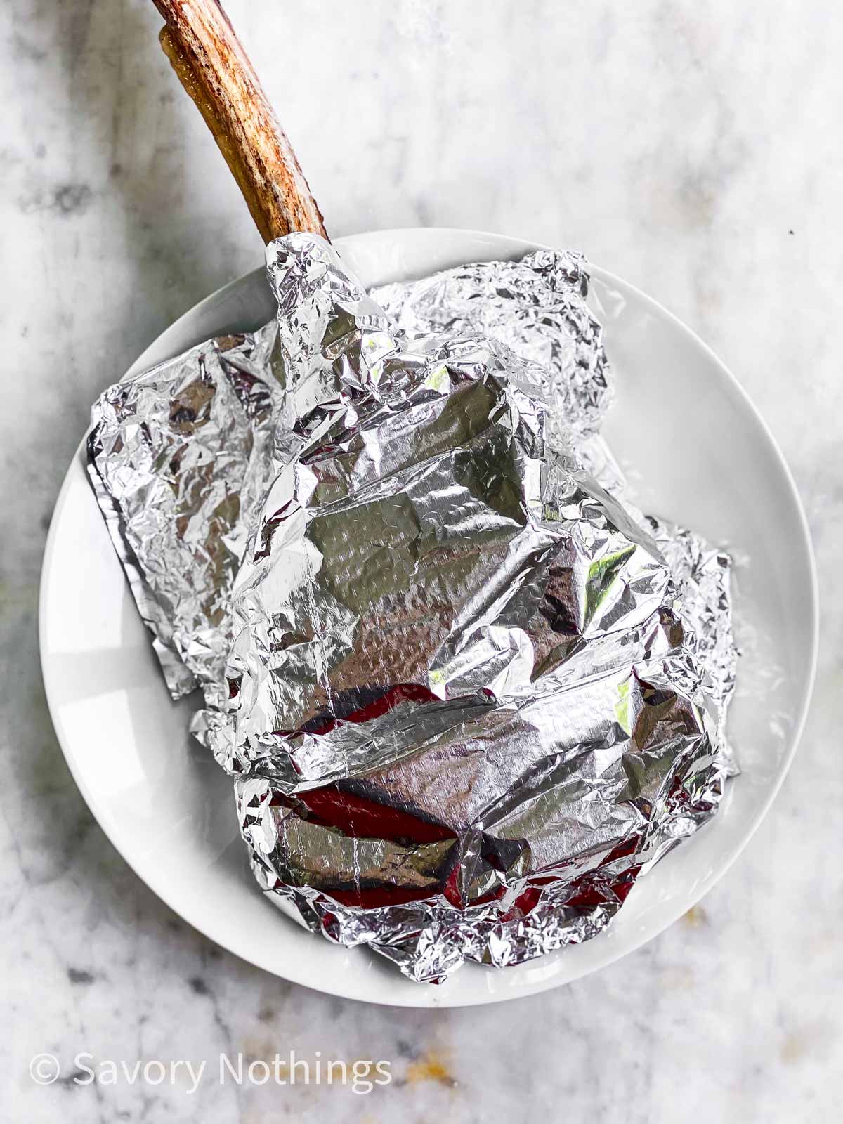 tomahawk steak covered with aluminium foil on white plate