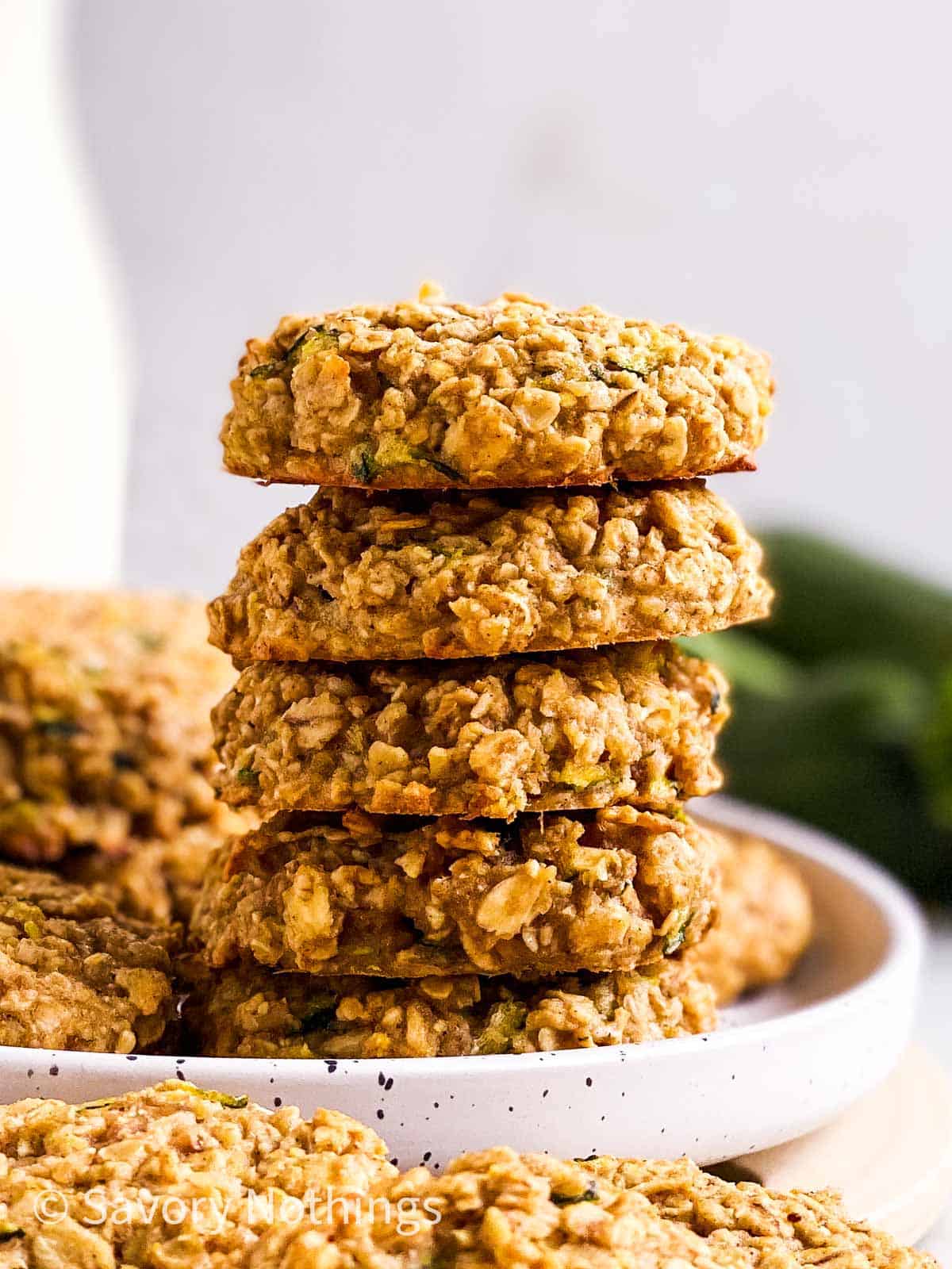 stack of zucchini bread breakfast cookies on white plate in front of milk bottle and fresh zucchini