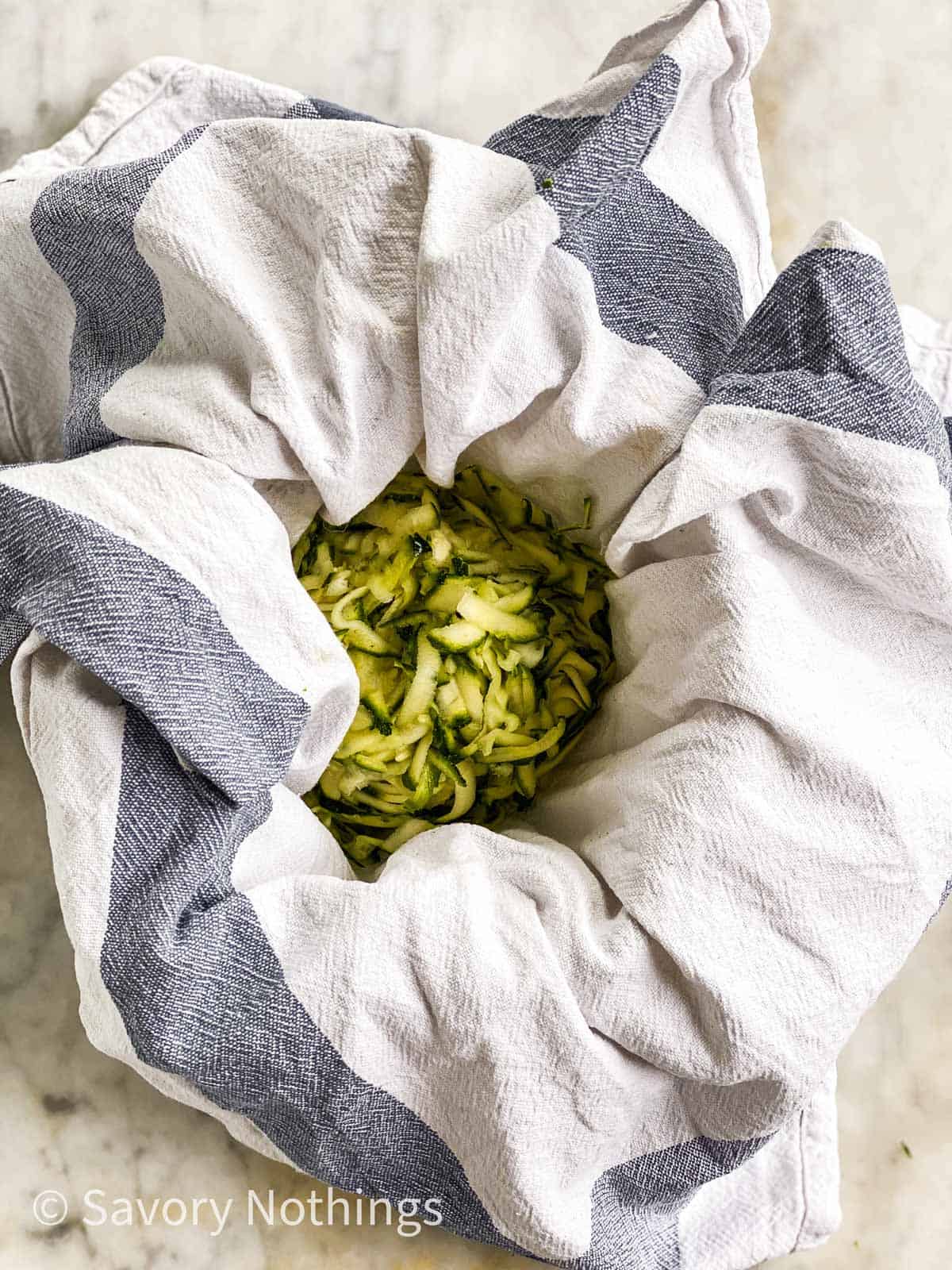 shredded zucchini nestled in middle of blue and white kitchen towel