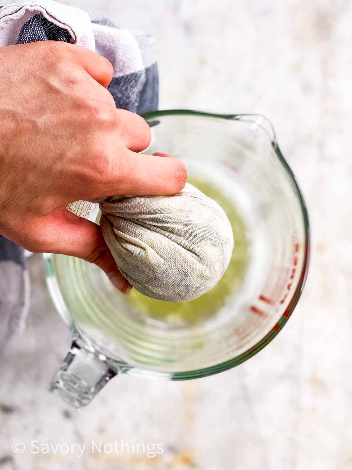 female hand squeezing zucchini in white kitchen towel over glass measuring jug